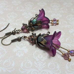 Mulberry purple bell flowers that have been hand painted with an iridescent green shimmer. They have antique bronze floral accents and light amethyst AB crystal drops from the bottoms of the flowers. They are fantasy vintage art nouveau in style.