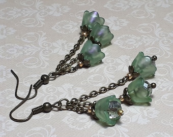Puede incluir: Un par de pendientes colgantes con una cadena y múltiples cuentas de flores de vidrio verde. Los pendientes tienen un acabado bronce.