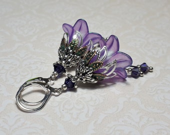 Puede incluir: Pendientes de flor morada con detalles plateados y verdes y cuentas de cristal morado.
