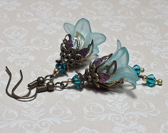 May include: A pair of dangle earrings with a light blue flower charm, bronze filigree, purple and gold accents, and teal blue crystal beads.