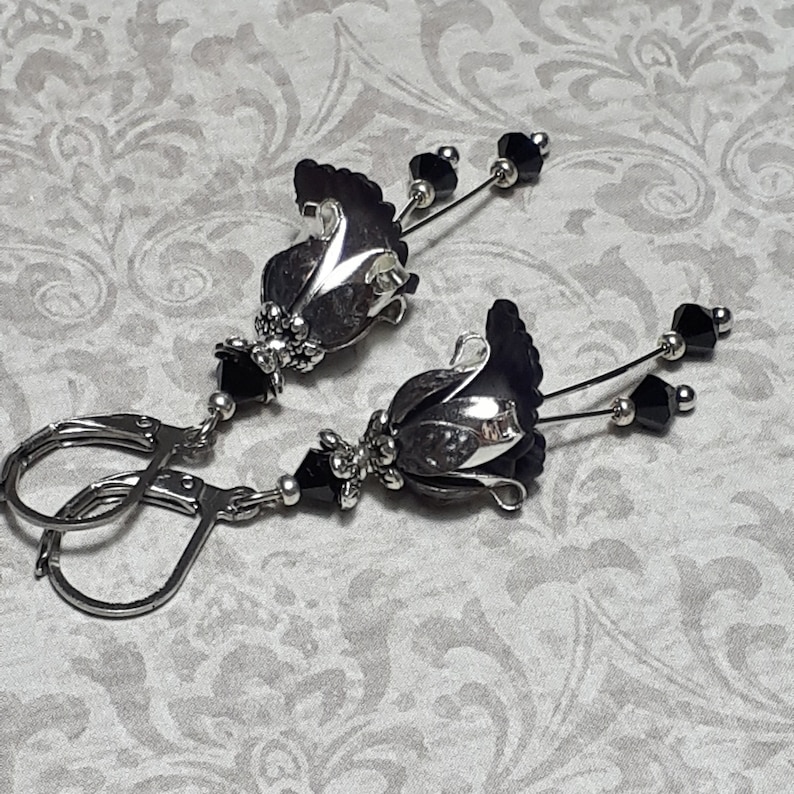 Gothic black vintage fairy flower earrings, delicate fluted flowers have been been paired with antique silver filigree floral bead caps. Jet black crystals are added to crystal drops that sway as the earrings move. Finished with lever back hooks.