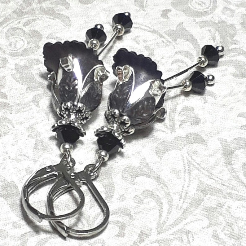 Gothic black vintage fairy flower earrings, delicate fluted flowers have been been paired with antique silver filigree floral bead caps. Jet black crystals are added to crystal drops that sway as the earrings move. Finished with lever back hooks.