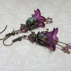 Mulberry purple bell flowers that have been hand painted with an iridescent green shimmer. They have antique bronze floral accents and light amethyst AB crystal drops from the bottoms of the flowers. They are fantasy vintage art nouveau in style.