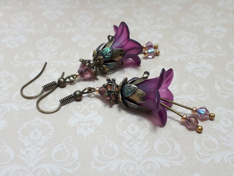 Mulberry purple bell flowers that have been hand painted with an iridescent green shimmer. They have antique bronze floral accents and light amethyst AB crystal drops from the bottoms of the flowers. They are fantasy vintage art nouveau in style.