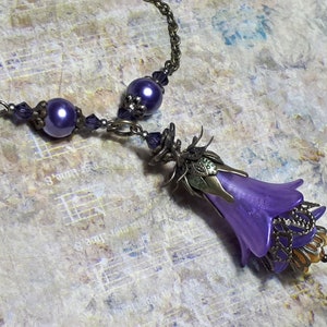 Vintage Style Deadly nightshade inspired necklace that has a purple flower drop with topaz yellow crystals and antique floral bead caps. It has a bronze chain that has purple pearls and crystals spaced along it. It has a whimsigoth style to it.