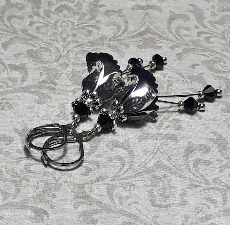 Gothic black vintage fairy flower earrings, delicate fluted flowers have been been paired with antique silver filigree floral bead caps. Jet black crystals are added to crystal drops that sway as the earrings move. Finished with lever back hooks.