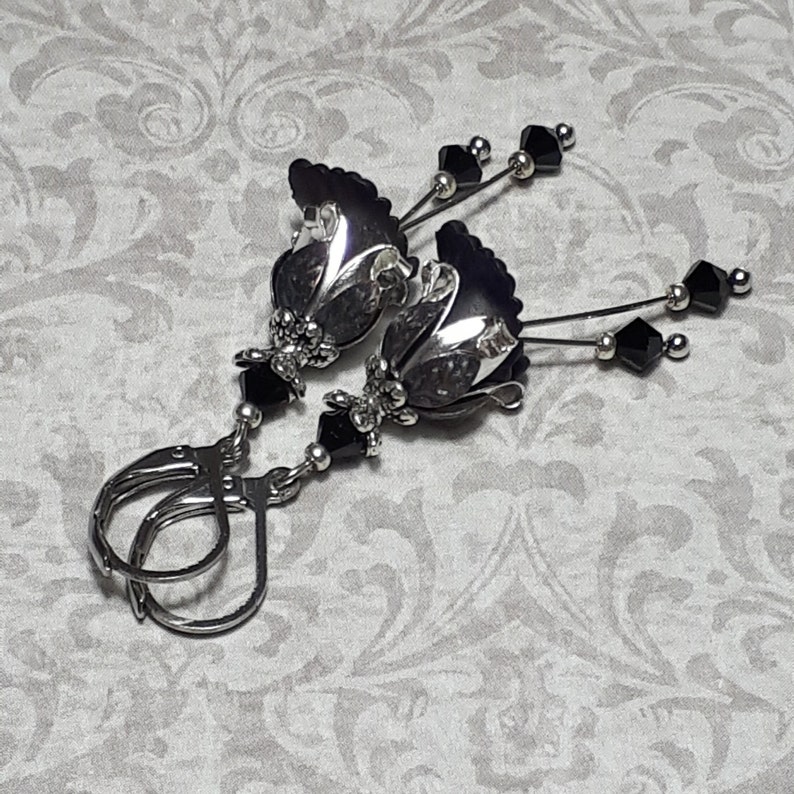 Gothic black vintage fairy flower earrings, delicate fluted flowers have been been paired with antique silver filigree floral bead caps. Jet black crystals are added to crystal drops that sway as the earrings move. Finished with lever back hooks.