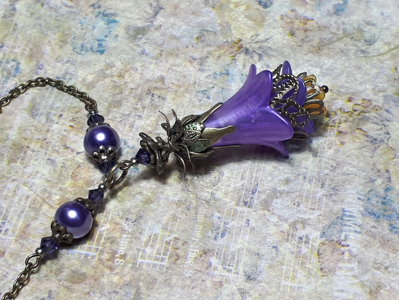 Vintage Style Deadly nightshade inspired necklace that has a purple flower drop with topaz yellow crystals and antique floral bead caps. It has a bronze chain that has purple pearls and crystals spaced along it. It has a whimsigoth style to it.