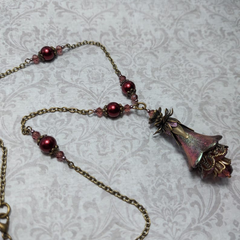 Crimson red and bronze gothic necklace. This handmade vintage style bronze necklace has a central flower drop that has been hand painted in colour shifting red and gold. Vibrant red glass pearls and burgundy crystals are added along the bronze tone chain. Whimsigoth jewelry, Fairytale fantasy necklace.
