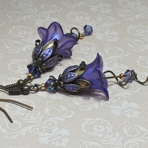 Deep purple bell flower earrings that have an iridescent finish and antique bronze metalwork. Purple faceted crystals are added above the flowers as well as on long metal spirals that hang from the bottom of the flowers. They have  floral bead caps.