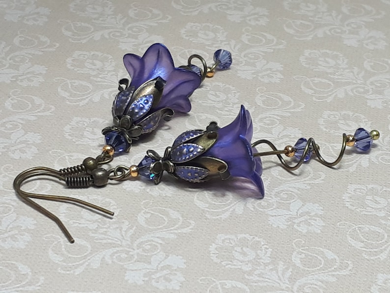 Deep purple bell flower earrings that have an iridescent finish and antique bronze metalwork. Purple faceted crystals are added above the flowers as well as on long metal spirals that hang from the bottom of the flowers. They have  floral bead caps.