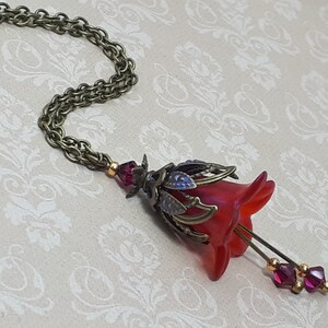 A red vintage style Lucite flower pendant necklace with a bronze filigree design and Siam red crystal beads that hang and sway from under the flowers. The necklace has a bronze tone chain. Fairycore style jewelry gift. Whimsical Necklace.
