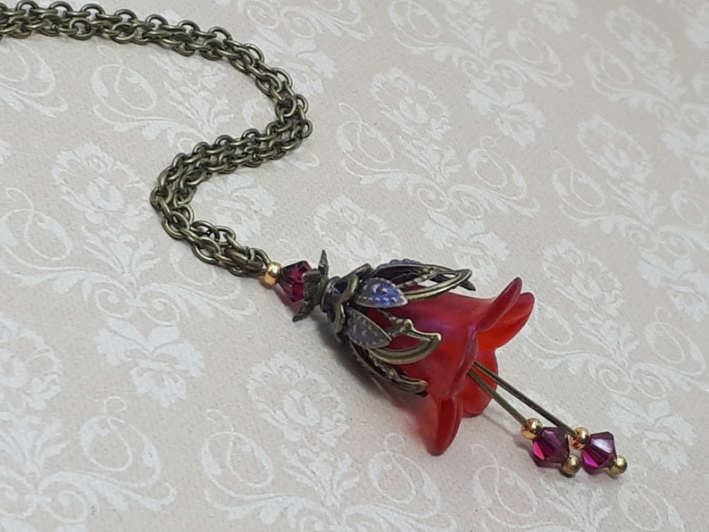 A red vintage style Lucite flower pendant necklace with a bronze filigree design and Siam red crystal beads that hang and sway from under the flowers. The necklace has a bronze tone chain. Fairycore style jewelry gift. Whimsical Necklace.
