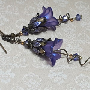 Deep purple bell flower earrings that have an iridescent finish and antique bronze metalwork. Purple faceted crystals are added above the flowers as well as on long metal spirals that hang from the bottom of the flowers. They have  floral bead caps.