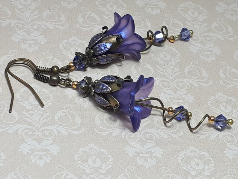 Deep purple bell flower earrings that have an iridescent finish and antique bronze metalwork. Purple faceted crystals are added above the flowers as well as on long metal spirals that hang from the bottom of the flowers. They have  floral bead caps.