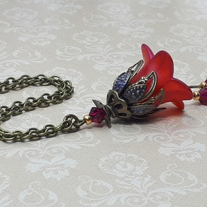 A red vintage style Lucite flower pendant necklace with a bronze filigree design and Siam red crystal beads that hang and sway from under the flowers. The necklace has a bronze tone chain. Fairycore style jewelry gift. Whimsical Necklace.