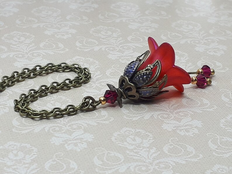 A red vintage style Lucite flower pendant necklace with a bronze filigree design and Siam red crystal beads that hang and sway from under the flowers. The necklace has a bronze tone chain. Fairycore style jewelry gift. Whimsical Necklace.
