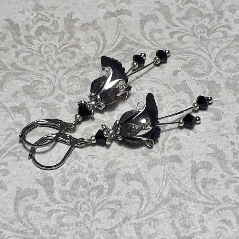 Gothic black vintage fairy flower earrings, delicate fluted flowers have been been paired with antique silver filigree floral bead caps. Jet black crystals are added to crystal drops that sway as the earrings move. Finished with lever back hooks.