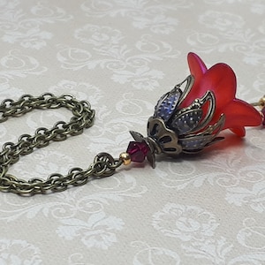 A red vintage style Lucite flower pendant necklace with a bronze filigree design and Siam red crystal beads that hang and sway from under the flowers. The necklace has a bronze tone chain. Fairycore style jewelry gift. Whimsical Necklace.