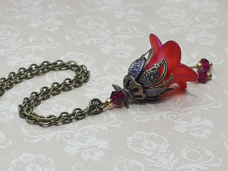 A red vintage style Lucite flower pendant necklace with a bronze filigree design and Siam red crystal beads that hang and sway from under the flowers. The necklace has a bronze tone chain. Fairycore style jewelry gift. Whimsical Necklace.