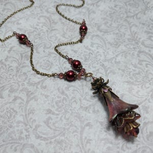 Crimson red and bronze gothic necklace. This handmade vintage style bronze necklace has a central flower drop that has been hand painted in colour shifting red and gold. Vibrant red glass pearls and burgundy crystals are added along the bronze tone chain. Whimsigoth jewelry, Fairytale fantasy necklace.