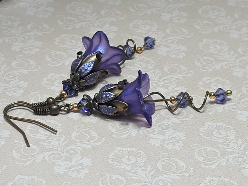 Deep purple bell flower earrings that have an iridescent finish and antique bronze metalwork. Purple faceted crystals are added above the flowers as well as on long metal spirals that hang from the bottom of the flowers. They have  floral bead caps.