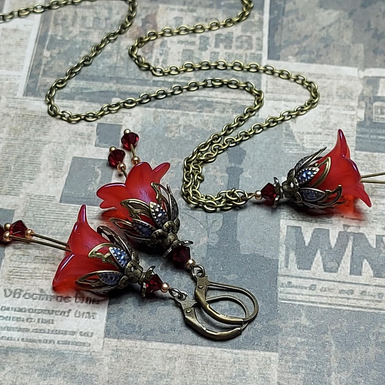 A red vintage style Lucite flower pendant necklace with a bronze filigree design and Siam red crystal beads that hang and sway from under the flowers. The necklace has a bronze tone chain. Fairycore style jewelry gift. Whimsical Necklace.