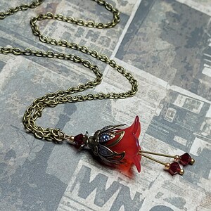 A red vintage style Lucite flower pendant necklace with a bronze filigree design and Siam red crystal beads that hang and sway from under the flowers. The necklace has a bronze tone chain. Fairycore style jewelry gift. Whimsical Necklace.