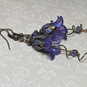 Deep purple bell flower earrings that have an iridescent finish and antique bronze metalwork. Purple faceted crystals are added above the flowers as well as on long metal spirals that hang from the bottom of the flowers. They have  floral bead caps.