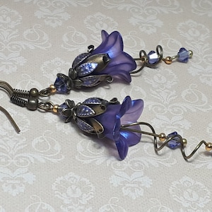 Deep purple bell flower earrings that have an iridescent finish and antique bronze metalwork. Purple faceted crystals are added above the flowers as well as on long metal spirals that hang from the bottom of the flowers. They have  floral bead caps.