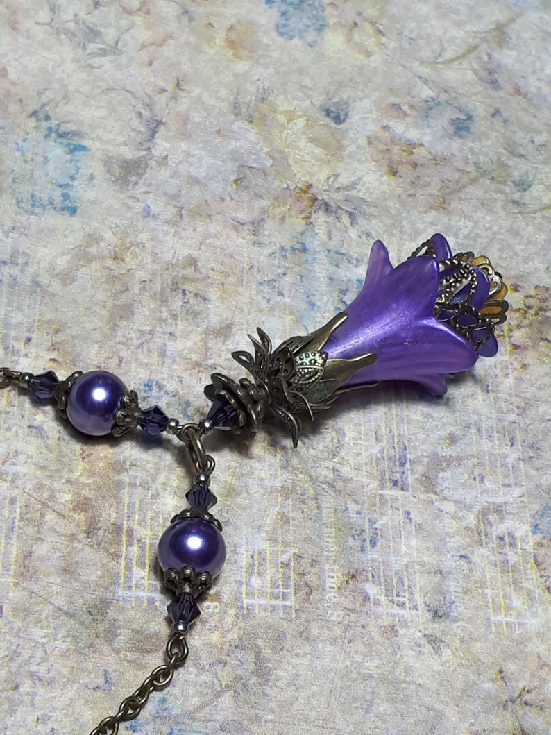 Vintage Style Deadly nightshade inspired necklace that has a purple flower drop with topaz yellow crystals and antique floral bead caps. It has a bronze chain that has purple pearls and crystals spaced along it. It has a whimsigoth style to it.