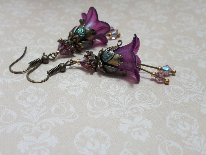 Mulberry purple bell flowers that have been hand painted with an iridescent green shimmer. They have antique bronze floral accents and light amethyst AB crystal drops from the bottoms of the flowers. They are fantasy vintage art nouveau in style.