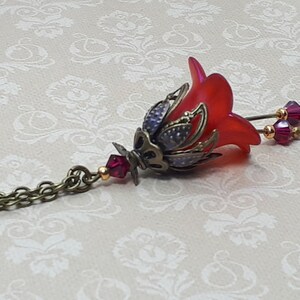 A red vintage style Lucite flower pendant necklace with a bronze filigree design and Siam red crystal beads that hang and sway from under the flowers. The necklace has a bronze tone chain. Fairycore style jewelry gift. Whimsical Necklace.
