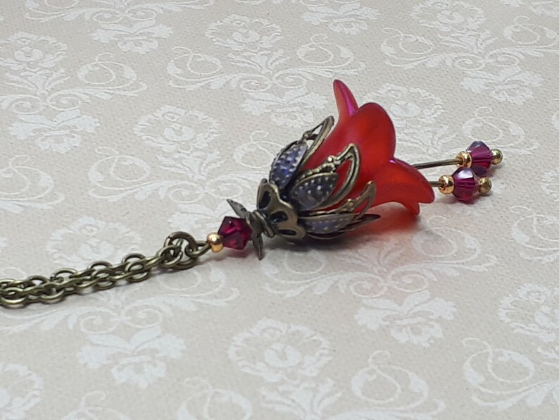 A red vintage style Lucite flower pendant necklace with a bronze filigree design and Siam red crystal beads that hang and sway from under the flowers. The necklace has a bronze tone chain. Fairycore style jewelry gift. Whimsical Necklace.