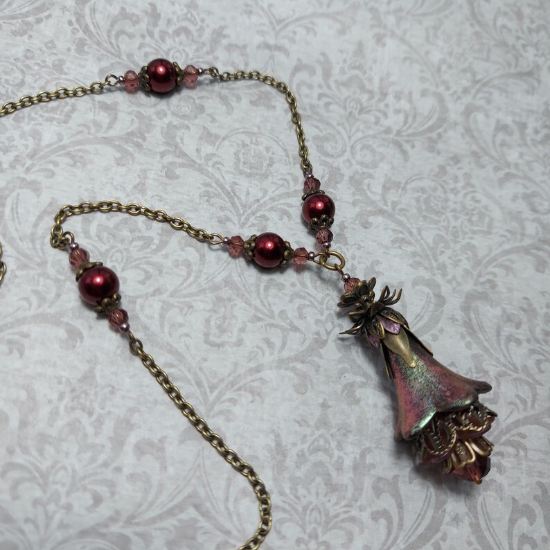 Crimson red and bronze gothic necklace. This handmade vintage style bronze necklace has a central flower drop that has been hand painted in colour shifting red and gold. Vibrant red glass pearls and burgundy crystals are added along the bronze tone chain. Whimsigoth jewelry, Fairytale fantasy necklace.