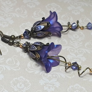 Deep purple bell flower earrings that have an iridescent finish and antique bronze metalwork. Purple faceted crystals are added above the flowers as well as on long metal spirals that hang from the bottom of the flowers. They have  floral bead caps.