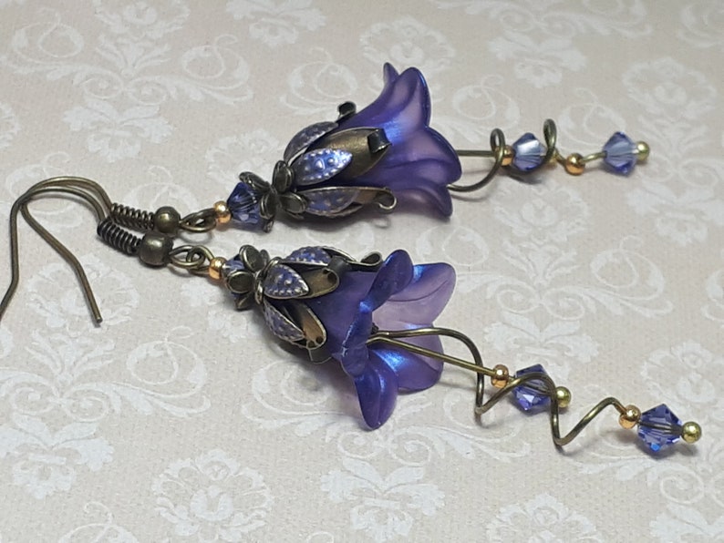 Deep purple bell flower earrings that have an iridescent finish and antique bronze metalwork. Purple faceted crystals are added above the flowers as well as on long metal spirals that hang from the bottom of the flowers. They have  floral bead caps.