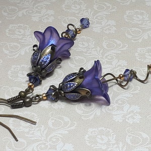 Deep purple bell flower earrings that have an iridescent finish and antique bronze metalwork. Purple faceted crystals are added above the flowers as well as on long metal spirals that hang from the bottom of the flowers. They have  floral bead caps.