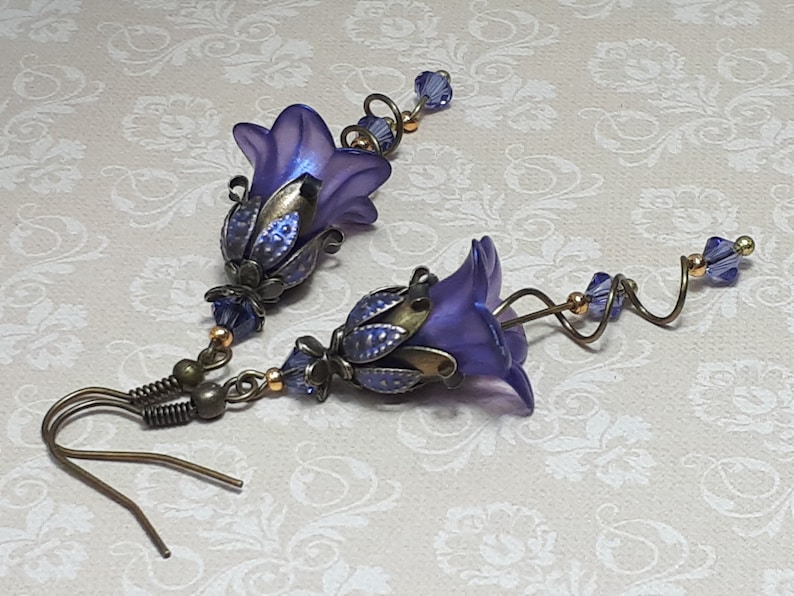 Deep purple bell flower earrings that have an iridescent finish and antique bronze metalwork. Purple faceted crystals are added above the flowers as well as on long metal spirals that hang from the bottom of the flowers. They have  floral bead caps.