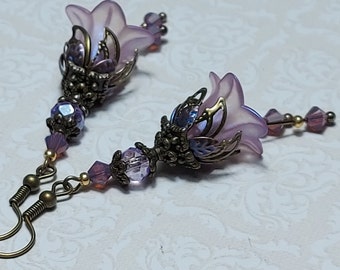May include: A pair of dangle earrings with a purple flower charm and crystal beads. The earrings have a bronze finish.