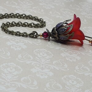 A red vintage style Lucite flower pendant necklace with a bronze filigree design and Siam red crystal beads that hang and sway from under the flowers. The necklace has a bronze tone chain. Fairycore style jewelry gift. Whimsical Necklace.