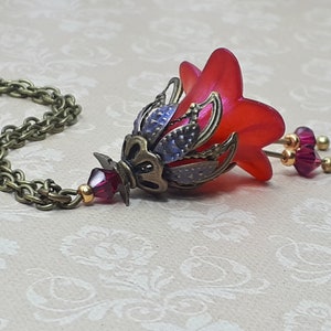 A red vintage style Lucite flower pendant necklace with a bronze filigree design and Siam red crystal beads that hang and sway from under the flowers. The necklace has a bronze tone chain. Fairycore style jewelry gift. Whimsical Necklace.