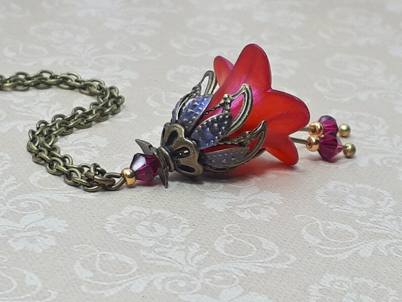 A red vintage style Lucite flower pendant necklace with a bronze filigree design and Siam red crystal beads that hang and sway from under the flowers. The necklace has a bronze tone chain. Fairycore style jewelry gift. Whimsical Necklace.