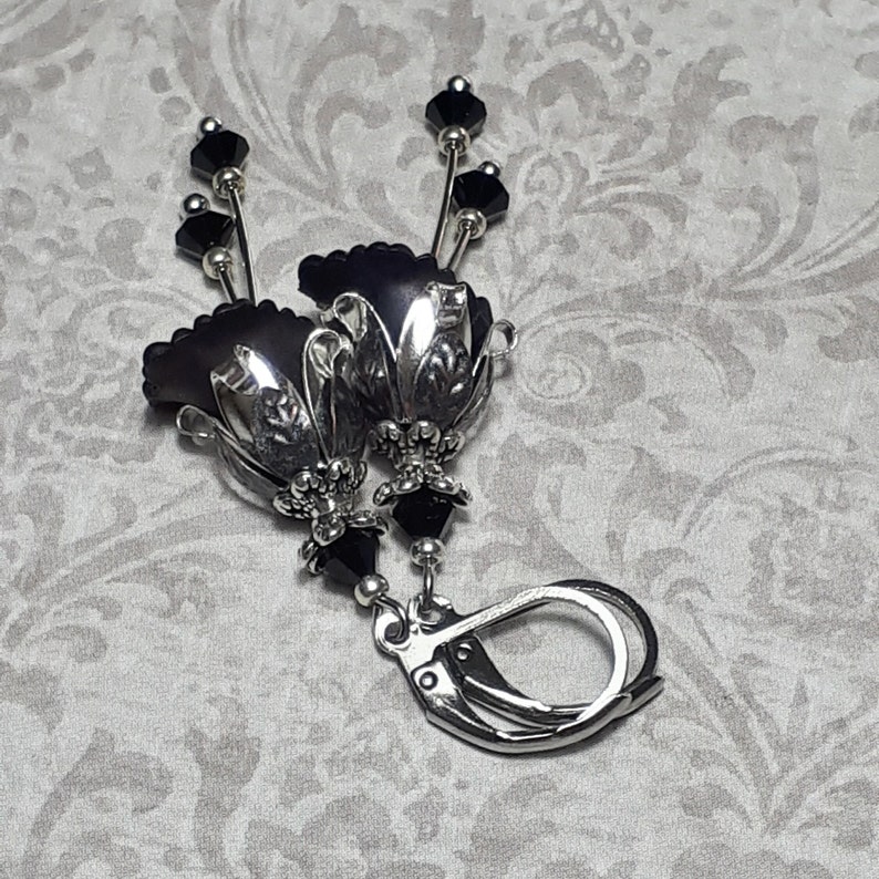 Gothic black vintage fairy flower earrings, delicate fluted flowers have been been paired with antique silver filigree floral bead caps. Jet black crystals are added to crystal drops that sway as the earrings move. Finished with lever back hooks.