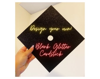 May include: Black glitter cardstock graduation cap with a white circle in the center and the text "Design your own!" in yellow neon lettering and "Blank Glitter Cardstock" in red neon lettering.