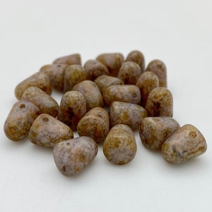 May include: A pile of brown and white speckled teardrop-shaped beads. The beads are made of glass and have a natural stone look.