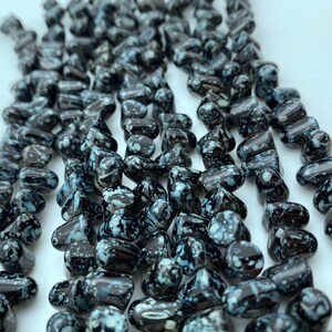 May include: A strand of black and white speckled glass beads. The beads are irregularly shaped and have a glossy finish.