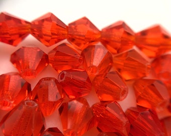 Op de afbeelding: Een close-up van een stapel oranje glazen kralen. De kralen zijn gefacetteerd en hebben een glanzende afwerking.