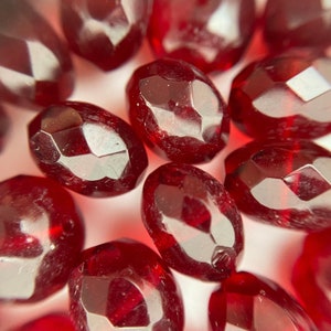 Könnte beinhalten: Nahaufnahme einer Gruppe roter Glasperlen mit facettiertem Design. Die Perlen sind oval geformt und haben eine glänzende, durchscheinende Oberfläche.