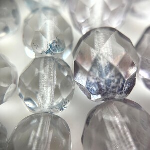 May include: Close-up of a strand of clear faceted glass beads. The beads have a slightly frosted appearance and are arranged in a line.